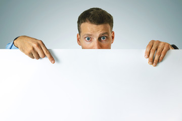 surprised man pointing on white blank poster with copy space