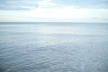 Obraz premium Beautiful white clouds on blue sky over calm sea with sunlight reflection, Tranquil sea harmony of calm water surface. Sunny sky and calm blue ocean.
