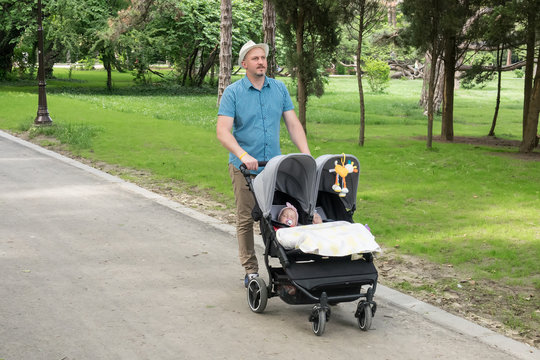 Father with kids in double stroller in a park.  Man pushing twins stroller, pram.