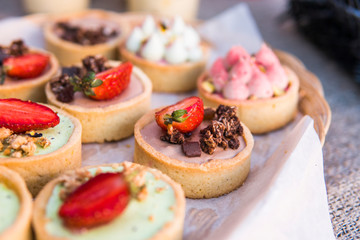 Background filled with colorful cakes and desserts with fresh fruits. Assorted different mini cakes with cream, chocolate and berries.
