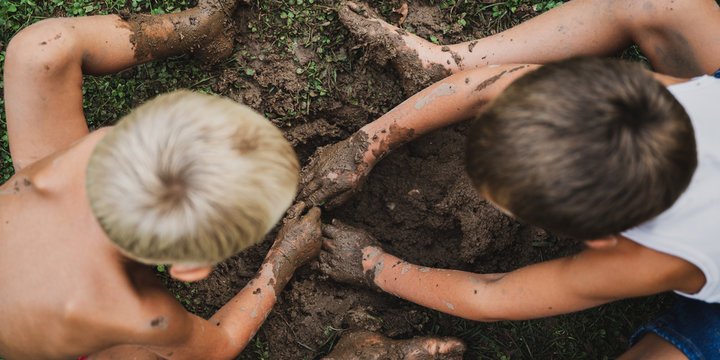 Toddler boys digging a muddy hole