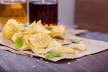 Potato chips with salt and greens on a table in a pub on a background of beer. Chips with greens as a snack to beer. October Beer Fest.