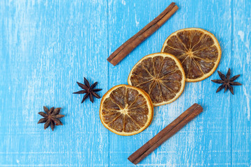 Dried slices of lemon, cinnamon and anise lie on a blue wooden background.