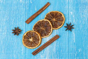 Dried slices of lemon, cinnamon and anise lie on a blue wooden background.