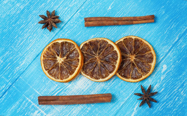 Dried slices of lemon, cinnamon and anise lie on a blue wooden background.