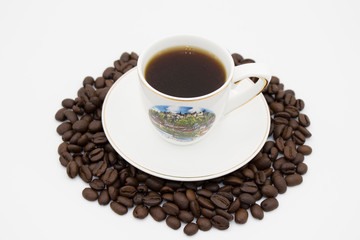 white Cup of coffee on a white plate surrounded by roasted coffee beans