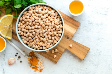 Dry uncooked chickpeas in a bowl, lemon, turmeric, spices, olive oil and coriander on a gray...