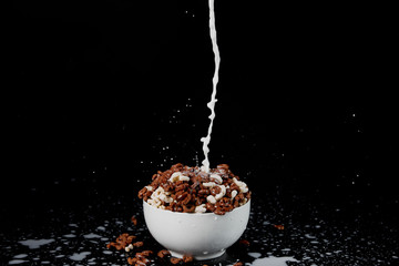 white bowl with assorted cereal with milk stream and splashes isolated on black