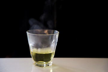 Smoke hot Chinese tea based on a transparent glass placed on a white table on a black background.