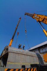 TWo truck cranes working over dry dock are lifting ship hull part