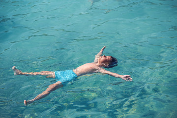 Healthy lifestyle. European boy in blue swim shorts swimming in blue clear sea water during his trip to Spain.