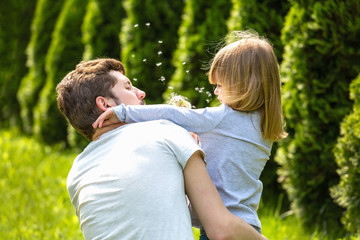 Back view. Father and daughter blowing dandelion flowers.