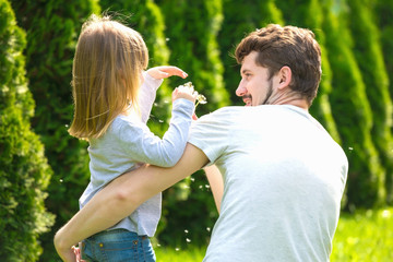 Happy family blowing dandelion flowers in summer garden