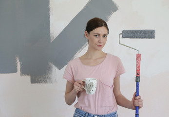 Portrait of a happy young woman holding paint applicator and a cup of coffee or tea, successful house refurbishment concept	