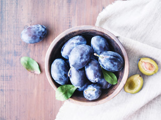 Fresh plums in a bowl on wooden table, soft focus, top view