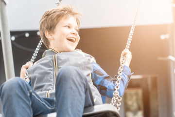 Cheerful, happy, naughty boy 9 years swinging on a swing in flight on the street.