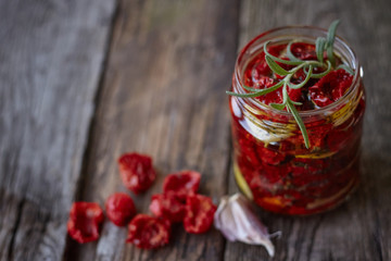 Close-up the jar of homemade sun-dried tomatoes with Provencal herbs, garlic and olive oil on a rustic wooden surface, selective focus