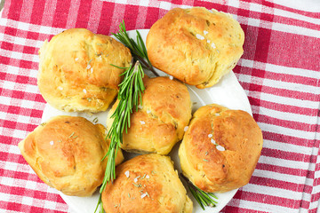 homemade fresh herb bread rolls of Provencal herbs with salt and a sprig branch of rosemary. Bread rolls bakery style on white plate and red and white towel in a cage italian style