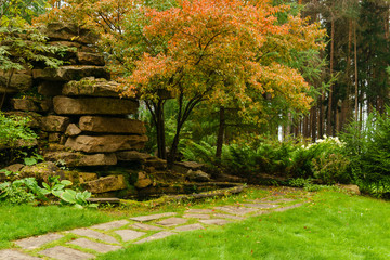 lawn among decorative bushes with a path and artificial rock made of stone slabs