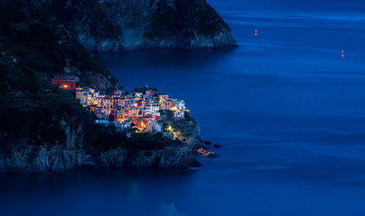 The fishing village of Manarola in Cinque Terre, Italy, illuminated at dusk during blue hour with the Mediterranean sea as background