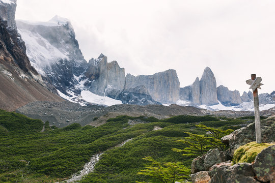 Vista view of mountain terrain with river, forest, and glacier, with wooden trail marker sign in foreground along W trek in Valle del Frances / French Valley in Torres del Paine, Patagonia, Chile