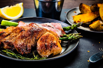 Grilled beefsteak with asparagus and baked potatoes on wooden background