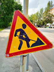 Road sign "Construction works". The symbol is old, scuffed and dirty. Paint yellow and red. The black man is digging.