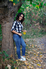 girl stands leaning against a tree with a yellow autumn leaf in her hand