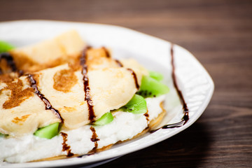 Crepes with kiwi and cream on wooden background