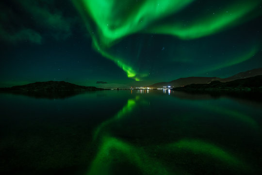 Green Northern lights reflecting in the lake with mountains and city in the background, Nuuk, Greenland