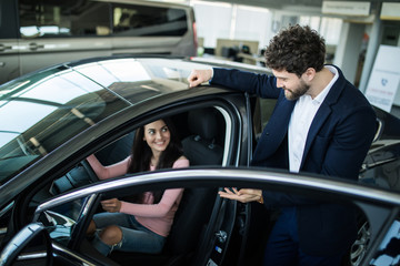 Plakat Beautiful young woman smiling while sitting in a new car in dealership