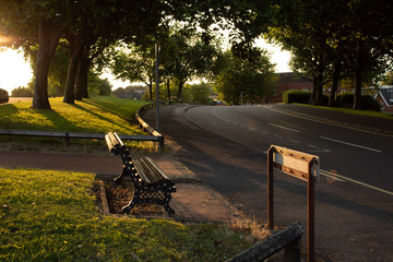 Bench and sign in front of a road during sunset