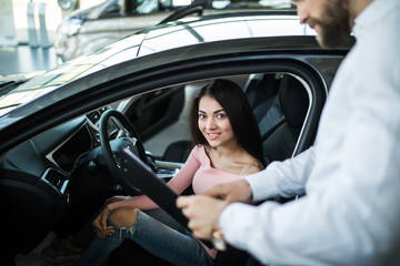 Fototapeta na wymiar Friendly vehicle dealer showing young woman new car in showroom