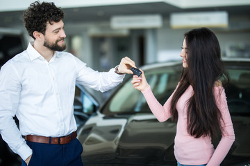 New car owners. Happy young woman buying a new car beautiful couple receiving car keys from a salesman at the car dealership