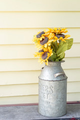 Sunflowers in Rustic Milk Jug on Yellow Porch of Farmhouse
