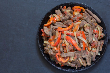 Top view of cooked liver with vegetables on frying pan on black background