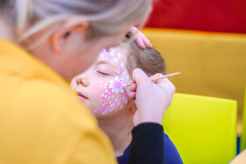  Stylish and trendy children's makeup.The master paints a beautiful figure on the face of a little...