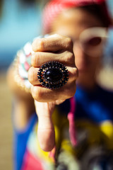 Closeup on pinup woman's hand showing thumb down, she has bad attitude and wearing big ring, bracelets, red bandana and sunglasses, colorful image retro style