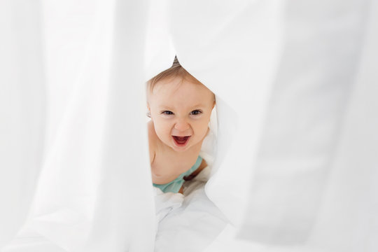 Laughing baby boy playing inside sheet on bed
