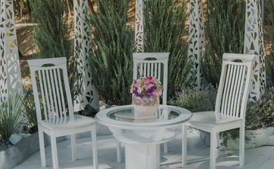 A recreation area in the park. White chairs and table with bouquet of flowers outdoor.