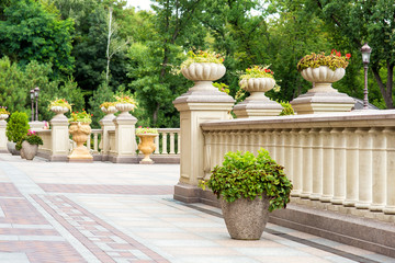 the back yard of a residential building with paving slabs and stone flowerpots on the walkway and on the railing pedestals with balustrades.