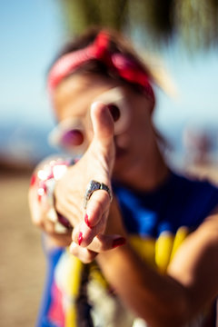 Closeup on pinup woman showing and pointing finger gun sign on a beach by a summer sunny day wearing red nail polish, rings, bracelets, red bandana and sunglasses, colorful image retro style
