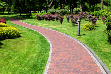 Footpath alley with a winding with a drainage system and ground lantern, a path leading into a park...