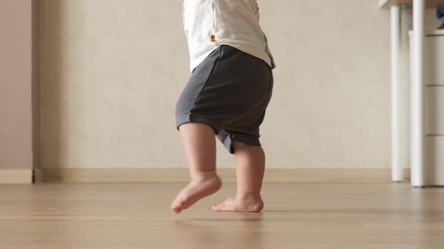 Baby boy takes first steps and learns how to walk barefoot at home. Slow motion