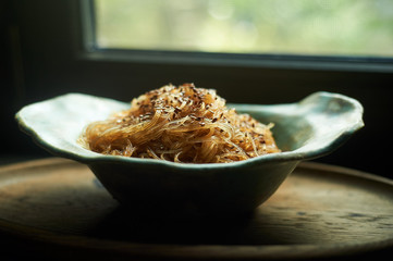 Cellophane with sesame seeds with sweet and sour sauce. In a deep ceramic bowl handmade. Appetizing dish