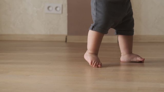 Baby boy takes first steps and learns how to walk barefoot at home. Slow motion