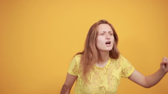 brunette girl in yellow t-shirt over isolated orange background shows emotions