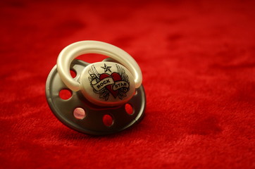 Baby dummy pacifier with the inscription rock star on a velvet red background