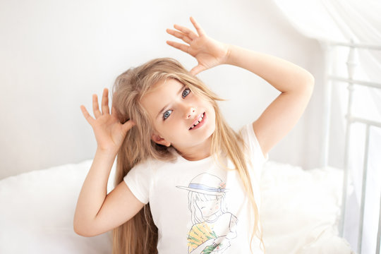 Portrait of a beautiful little girl with long curly hair, smiling at the camera, making funny faces. Cute funny charming joyful blond little girl with eyes wide open smiles. Childhood concept. morning