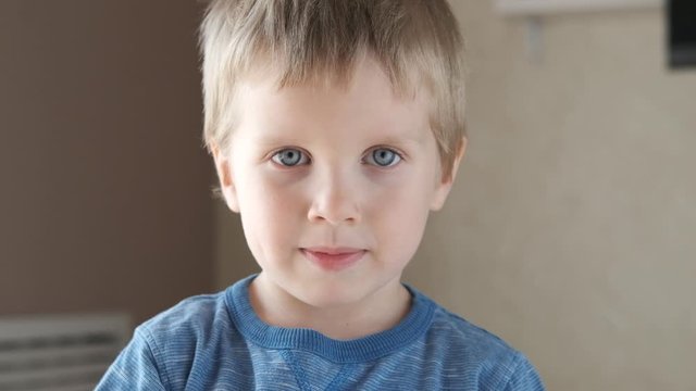 Adorable happy kid baby boy is looking to the camera. Baby looks around and then smiles and laughs. 4 year old fair-haired child with blue eyes smiles at home. Slow motion